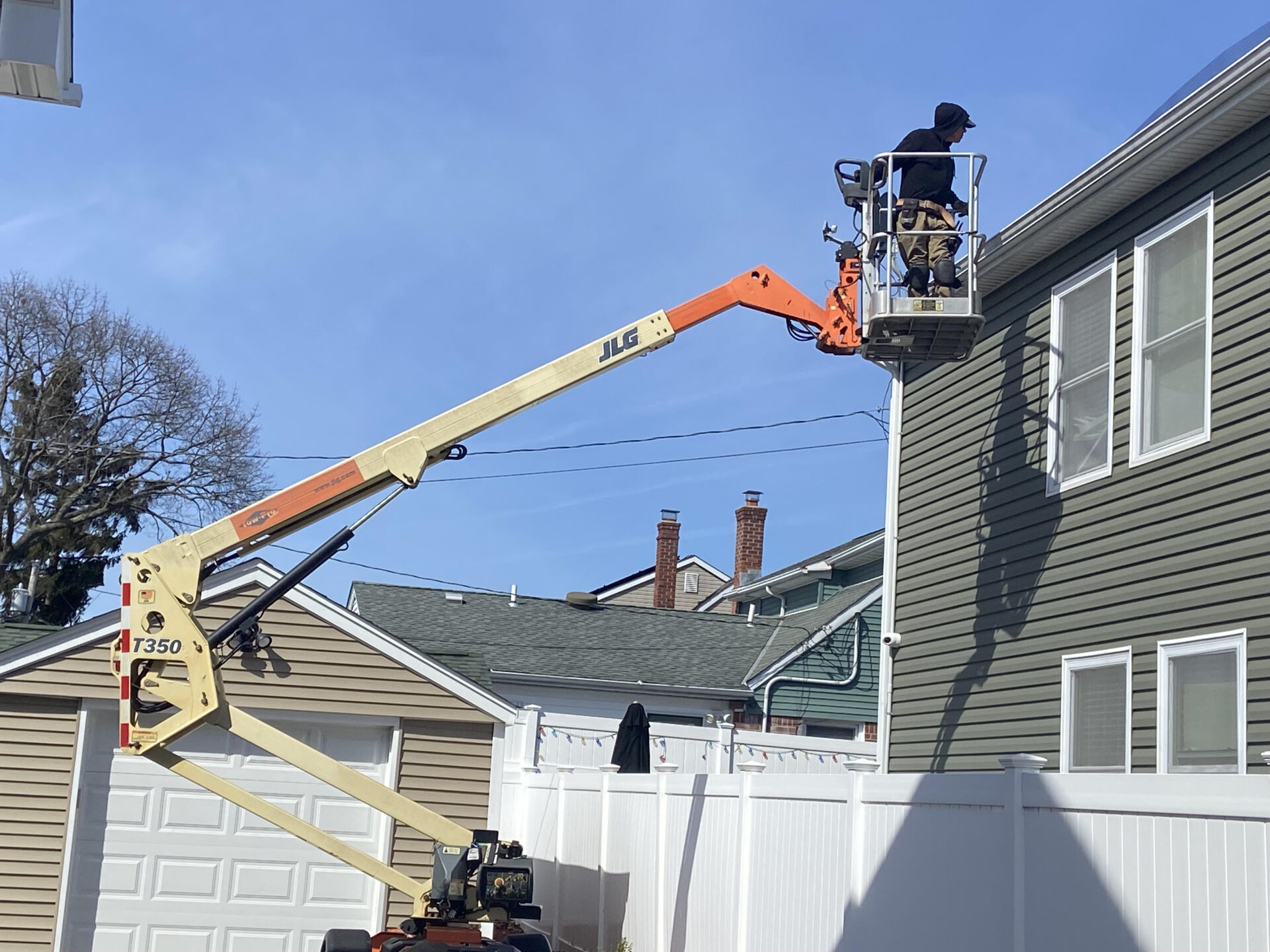 Worker on boom lift repairing house siding